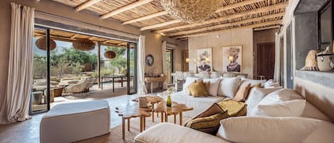 A spacious living area with a large sofa, a dining table, and a view through a glass door to an outdoor patio.