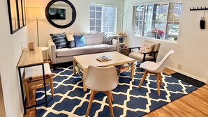 A modern living room with a sofa, coffee table, and chairs, a TV, and a large window with a view. - NEW! Peaceful Bungalow • Close to Lightrail • Yard (Seattle)