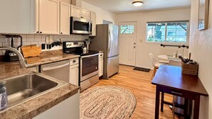 A kitchen with white cabinets, stainless steel appliances, a granite countertop, and a wooden floor. - NEW! Peaceful Bungalow • Close to Lightrail • Yard (Seattle)