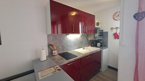 Eine kleine Küche mit roten Schränken, einer Spüle, einer Mikrowelle und einer Kaffeemaschine.