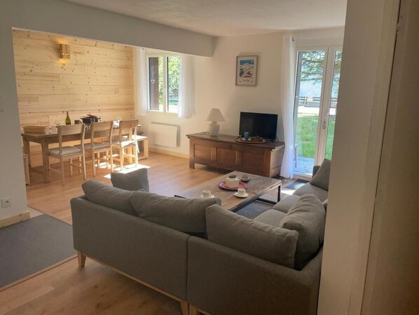A living room with a sofa, a coffee table, a TV, and a dining area with chairs and a table. - Ground floor, tv, 80m², Pra Loup (Pra Loup)