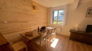 A wooden interior with a dining table, chairs, a small stool, a window with a view, and a lamp. - 100m from ski slopes, Ground floor, tv, 80m², Pra Loup (Pra Loup)