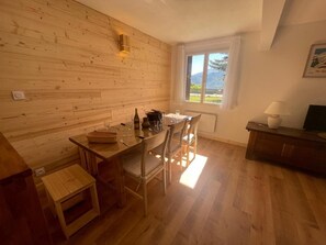 A wooden interior with a dining table, chairs, a small stool, a window with a view, and a lamp. - Ground floor, tv, 80m², Pra Loup (Pra Loup)
