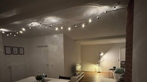 Un comedor con una mesa y sillas blancas, una pared de ladrillo y luces colgantes en el techo.