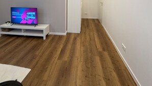 Una habitación moderna y luminosa con suelo de madera, un mueble de entretenimiento blanco y un televisor.