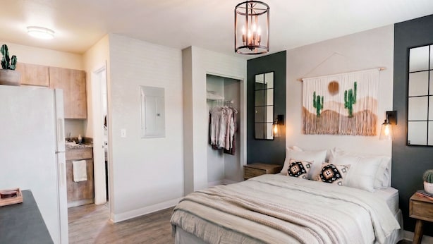 Un dormitorio con cama, mesitas de noche, lámpara colgante, espejo, puerta y una pequeña planta en maceta.