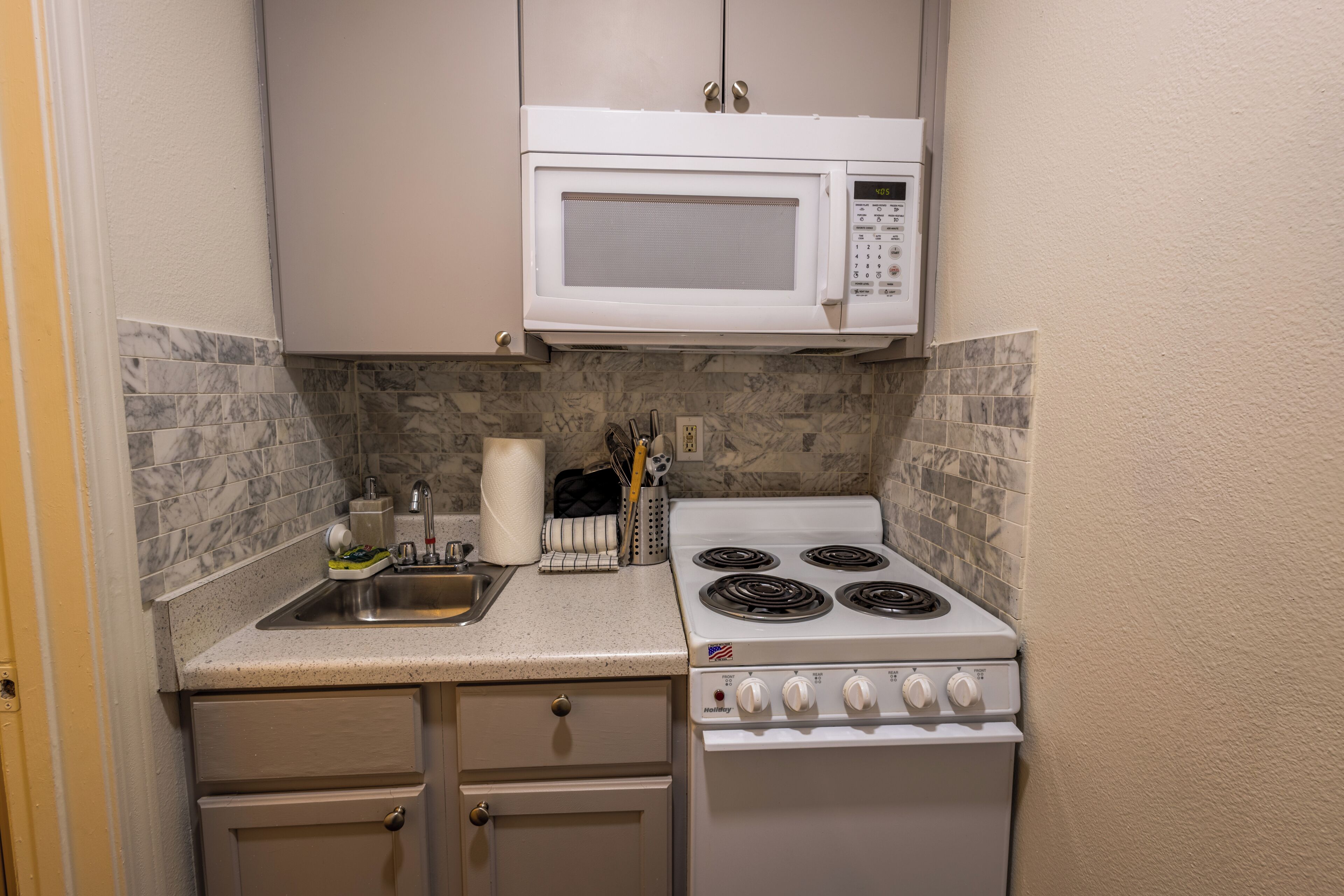 A compact kitchen with a white microwave, stove, and sink.