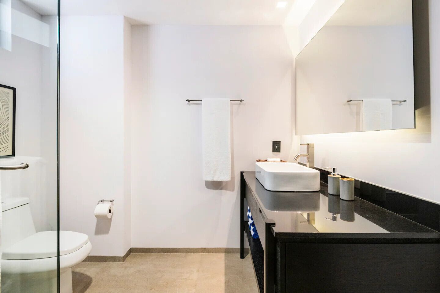 Ein modernes Badezimmer mit Duschkabine aus Glas, einer weißen Toilette, einem schwarzen Waschtisch mit weißem Waschbecken und einem großen Spiegel.