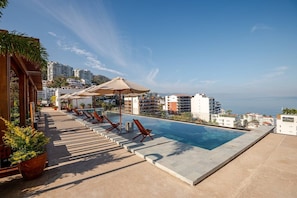 Ein Poolbereich mit Liegestühlen, Sonnenschirmen und Blick auf das Meer und Gebäude.