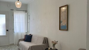 Ein Zimmer mit einem Bett, einem kleinen Tisch mit einer Vase, einem Bild an der Wand und einem Fenster mit Vorhängen.