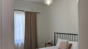 Ein Schlafzimmer mit einem Bett, einem Nachttisch, einer Lampe und einem Fenster mit Vorhängen.