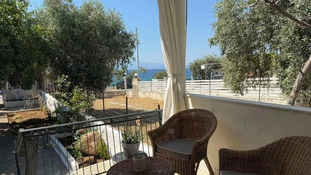 Ein Balkon mit Korbmöbeln, einer Topfpflanze und Blick auf das Meer.