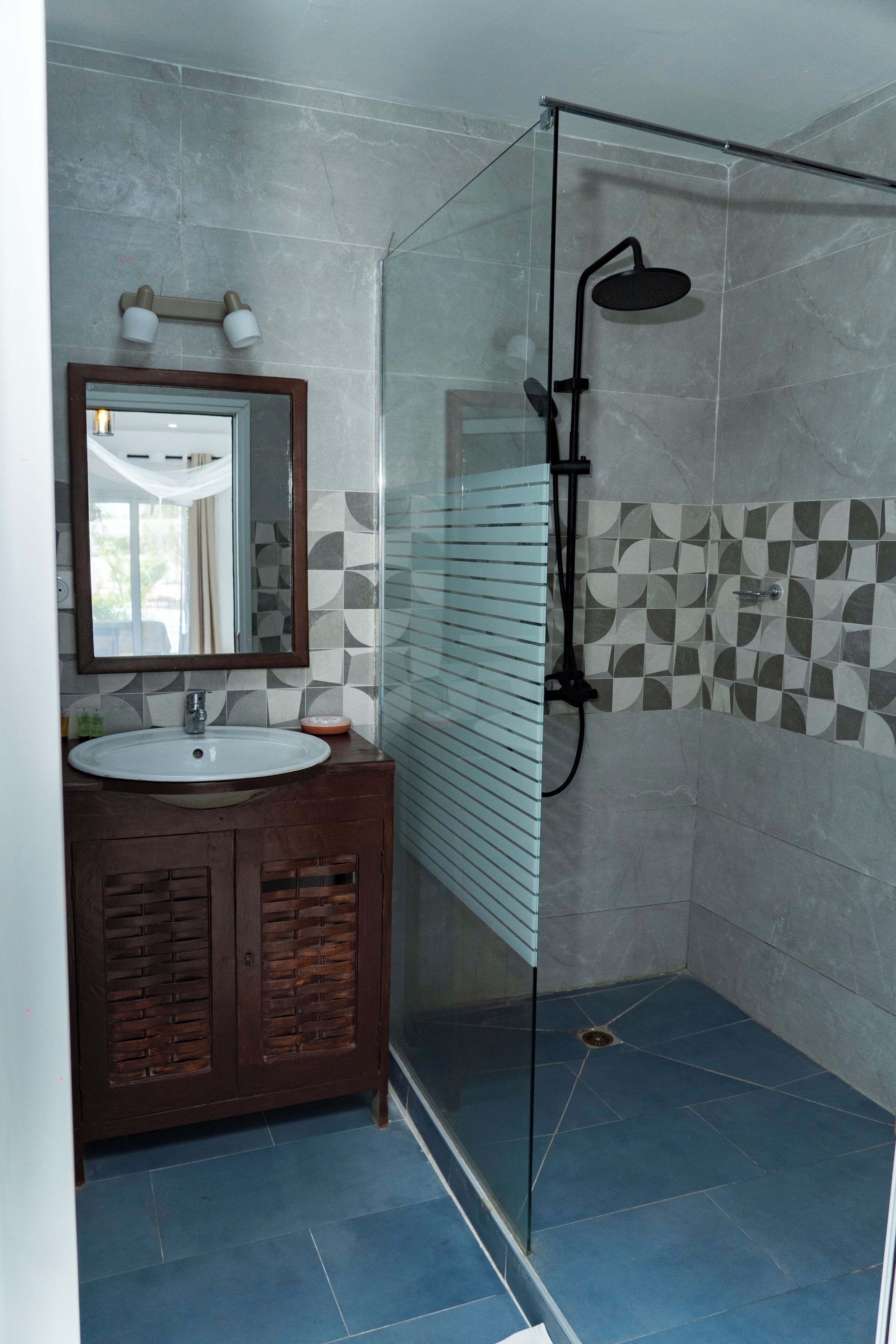 Une salle de bain avec une douche à parois de verre, un lavabo avec un miroir et des carreaux décoratifs sur les murs.