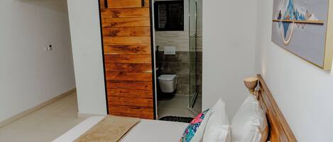 Un dormitorio con cama, puerta corredera de madera, ducha y una obra de arte colgada en la pared.