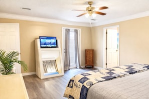 A bedroom with a bed, a television on a stand, a ceiling fan, and a door. - Beach Retreat, Dog-Friendly, Fenced Yard, Fireplace, Near Ferry (Dauphin Island)