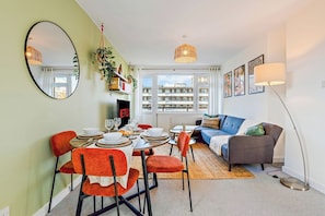 A dining area with a table set for four, a sofa, a floor lamp, and a large mirror on the wall. - Spacious 2-Bed Apartment In Hackney (Greater London)