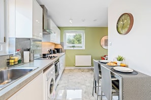 A modern kitchen with a dining area, stainless steel appliances, and a view of greenery outside. - Spacious 2-Bed Apartment In Hackney (Greater London)