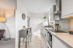 A modern kitchen with a dining area, a washing machine, and a visible door leading to another room. - Spacious 2-Bed Apartment In Hackney (Greater London)