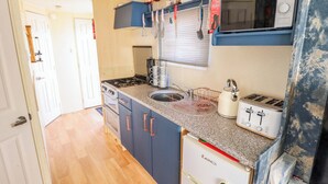 A compact kitchen with a stove, sink, and a microwave. There are cabinets and a refrigerator. - 517 - Promenade Caravan Site (Skegness)