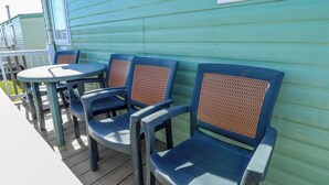 A deck with plastic chairs and a small round table. - 517 - Promenade Caravan Site (Skegness)