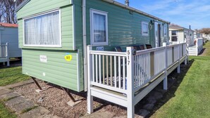 A green mobile home with a white porch, numbered 517, and a small deck. - 517 - Promenade Caravan Site (Skegness)