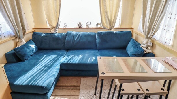 A room with a blue sofa, a glass-top table, and curtains. - 517 - Promenade Caravan Site (Skegness)