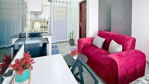 En kompakt opholdsstue med spiseplads, en rød sofa og et tekøkken.