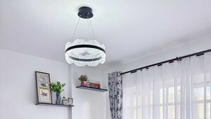 Et soveværelse med seng, sengebord, stol, loftlampe og et vindue med gardiner.
