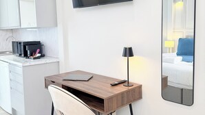 Una habitación de hotel moderna con un escritorio de madera, una silla, un televisor de pantalla plana, una lámpara de noche y un espejo grande que refleja la cama y la habitación.