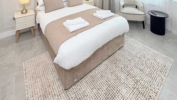 Ein modernes Hotelzimmer mit einem großen Bett, Nachttischen, einem Sessel und Blick auf die Stadt durch große Fenster.