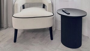 Een moderne stoel met zwarte accenten en een kleine ronde tafel met een afstandsbediening.