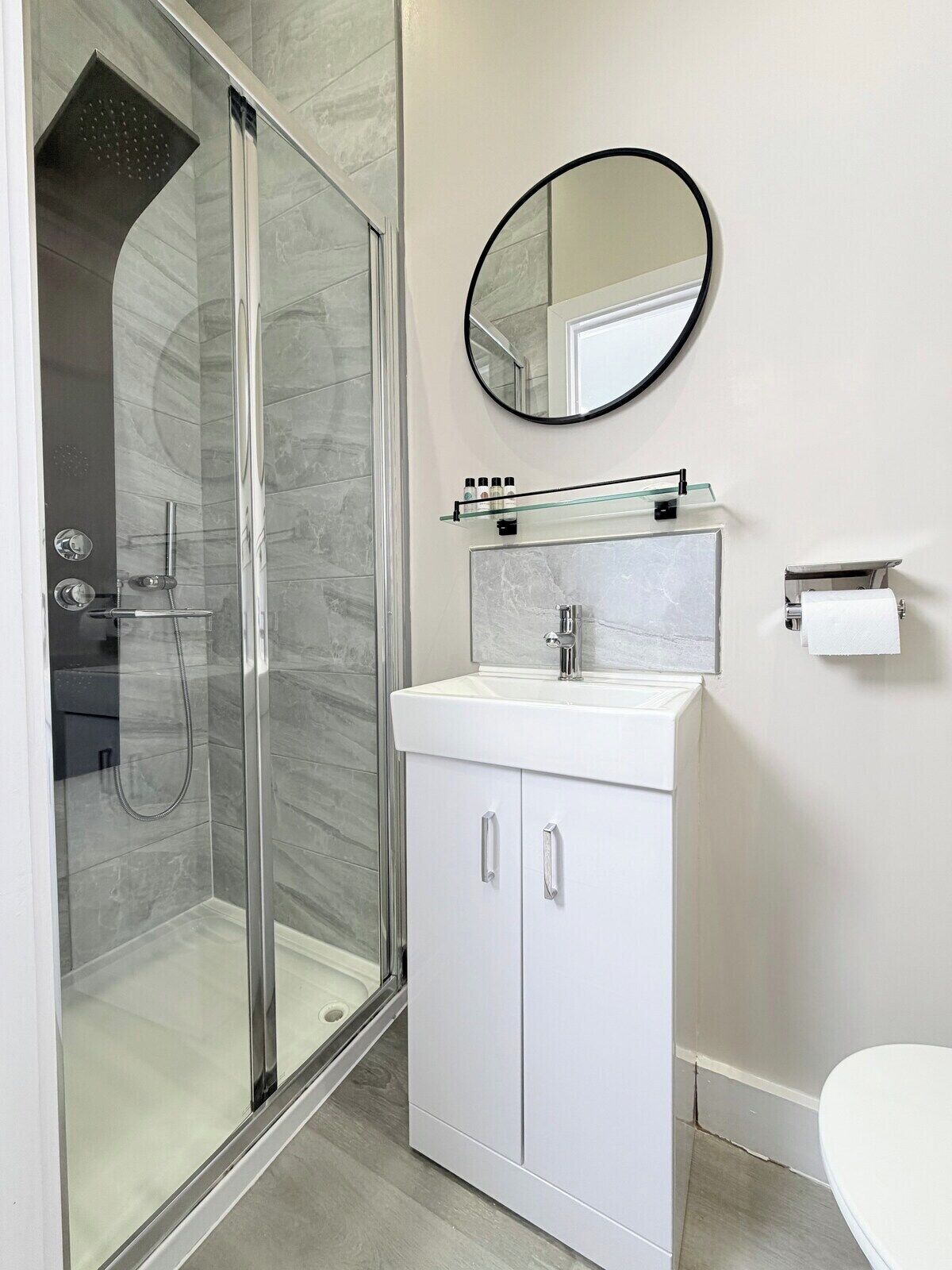 Un baño moderno con cabina de ducha de vidrio, un lavabo blanco con espejo superior y un inodoro.