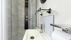 Ein modernes Badezimmer mit einer gl äsernen Duschkabine, einem weißen Waschbecken mit Chromarmatur und einem Handtuchhalter.