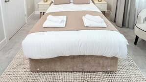 Ein ordentlich eingerichtetes Hotelzimmer mit einem großen Bett, zwei Nachttischen mit Lampen, einem Kopfteil und zwei gerahmten Bildern an der Wand.