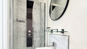 Un baño moderno con ducha envuelta en vidrio, un lavabo blanco con espejo y un respaldo de mármol.