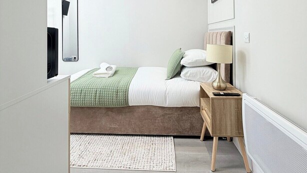 Un dormitorio moderno con cama, mesita de noche, lámpara y un cuadro en la pared.
