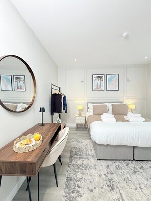 Een moderne hotelkamer met een houten bureau, een bed met een grijs hoofdeinde, een ronde spiegel en twee nachtkastjes met lampen.