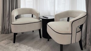 Une pièce avec deux fauteuils blancs, une petite table ronde et des rideaux légers.
