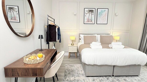 Une chambre d’hôtel moderne équipée d’un lit, d’un bureau, d’une chaise et d’un grand miroir.