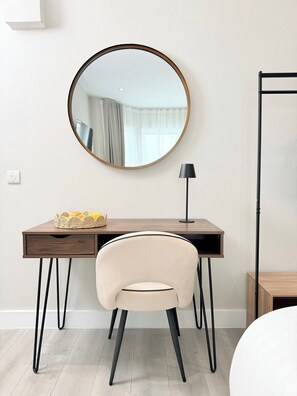 Quarto moderno com um espelho redondo, uma escrivaninha com cadeira, abajur e luminária de chão.