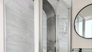 Une salle de bain moderne avec une douche à parois de verre, un lavabo blanc et un miroir rond.