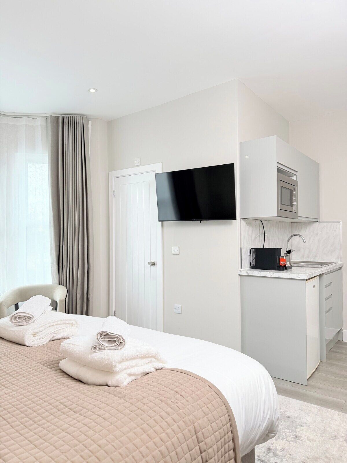 Een moderne hotelkamer met een bed, een flatscreen-tv, een ingebouwde magnetron en een kleine kitchenette.