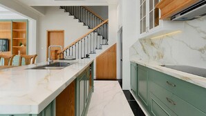 Uma cozinha moderna com bancada de mármore, armários verdes e uma escada que leva a outro nível.
