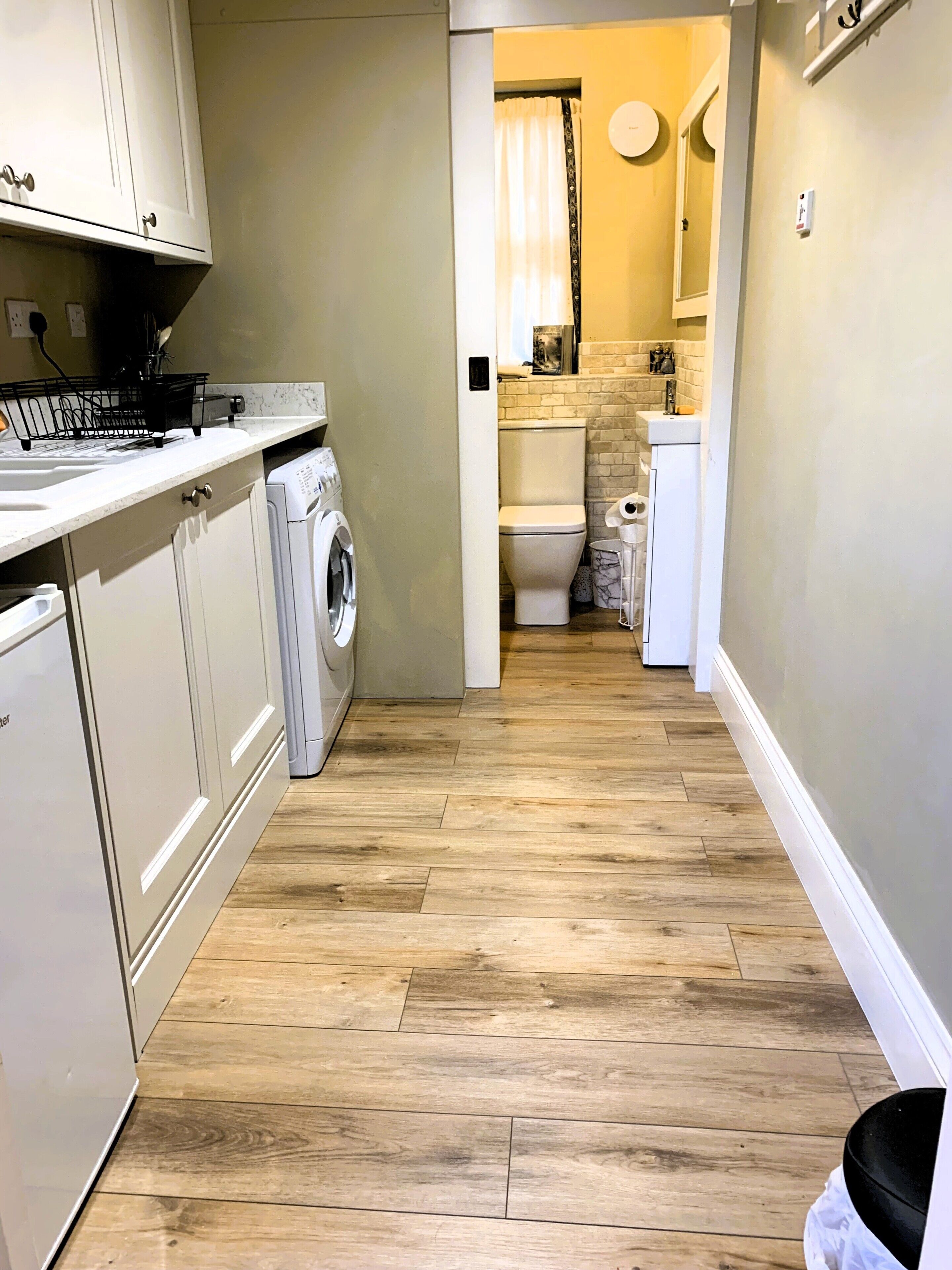 A narrow hallway with a washing machine, a sink, and a toilet.