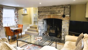 A living room with a stone fireplace, a sofa, a glass coffee table, and a television. - Stylish Retreat in the Heart of Somerton with Wood Fire (Somerton)
