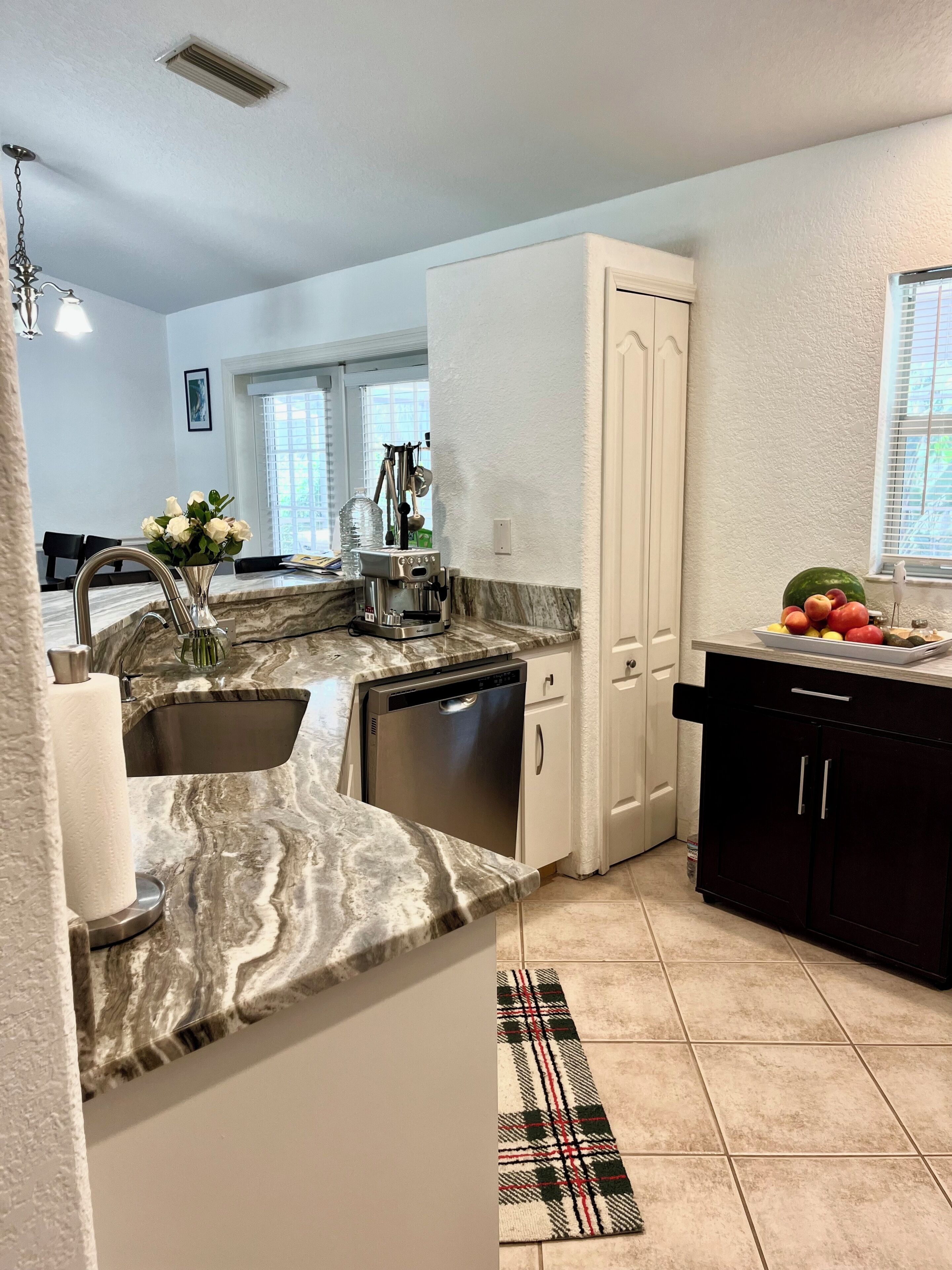 A kitchen with a marble countertop, a dishwasher, a coffee maker, and a fruit bowl.