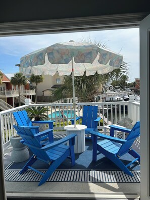 A balcony with blue chairs and a table, overlooking a pool and a building with a colorful umbrella. - Charming 2-bedroom condo in SUPERB Orange Beach! (Orange Beach)