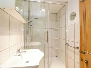 A bathroom with a glass-enclosed shower, a white sink, and a wooden door. - St. Dominic Cottage (St Ives)