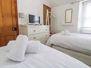 A bedroom with a bed, a dresser with a television, a mirror, and a door. - St. Dominic Cottage (St Ives)