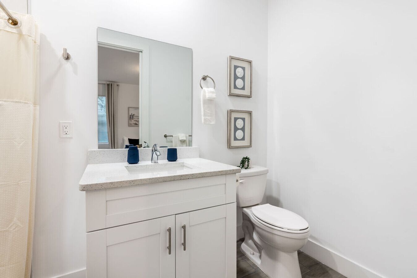 A bathroom with a white vanity, a mirror, a toilet, and two framed pictures on the wall.